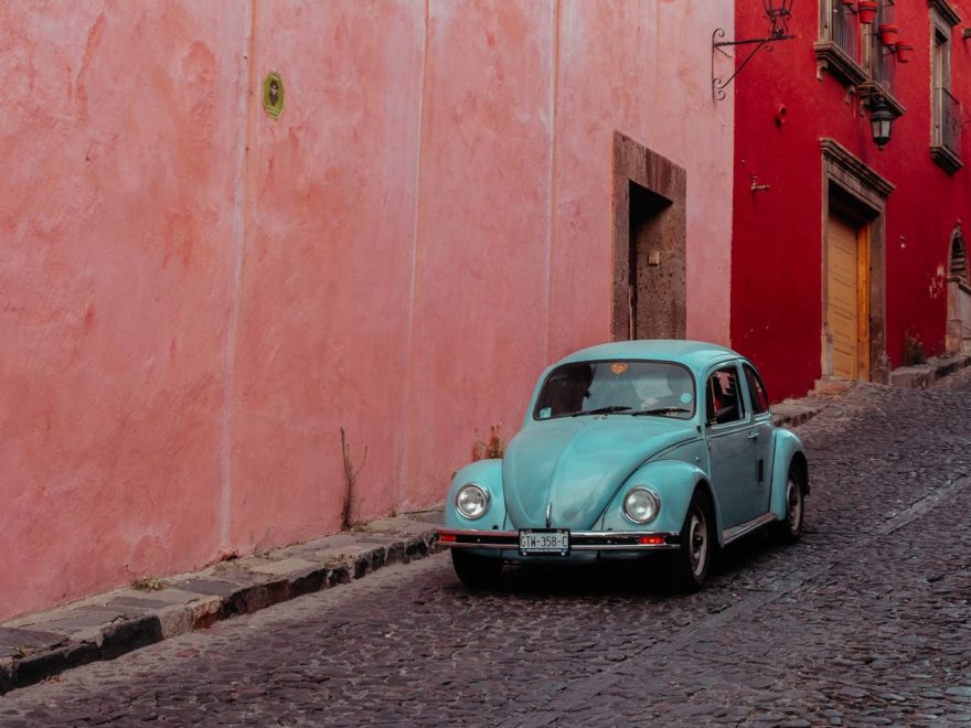 turquoise buggy moving along street with pink and red buildings