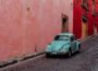 turquoise buggy moving along street with pink and red buildings