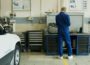 man in blue overall beside white car in service garage